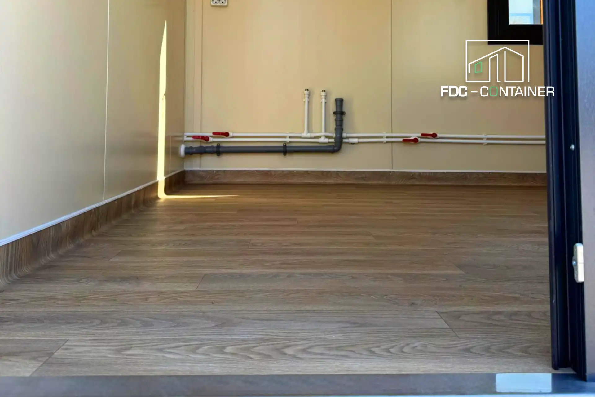 Innenraum im Sanitärcontainer mit Wasserleitungen und Holzoptik-Boden – FDC Container Innenraum im Sanitärcontainer mit Wasserleitungen und Holzoptik-Boden – FDC Container