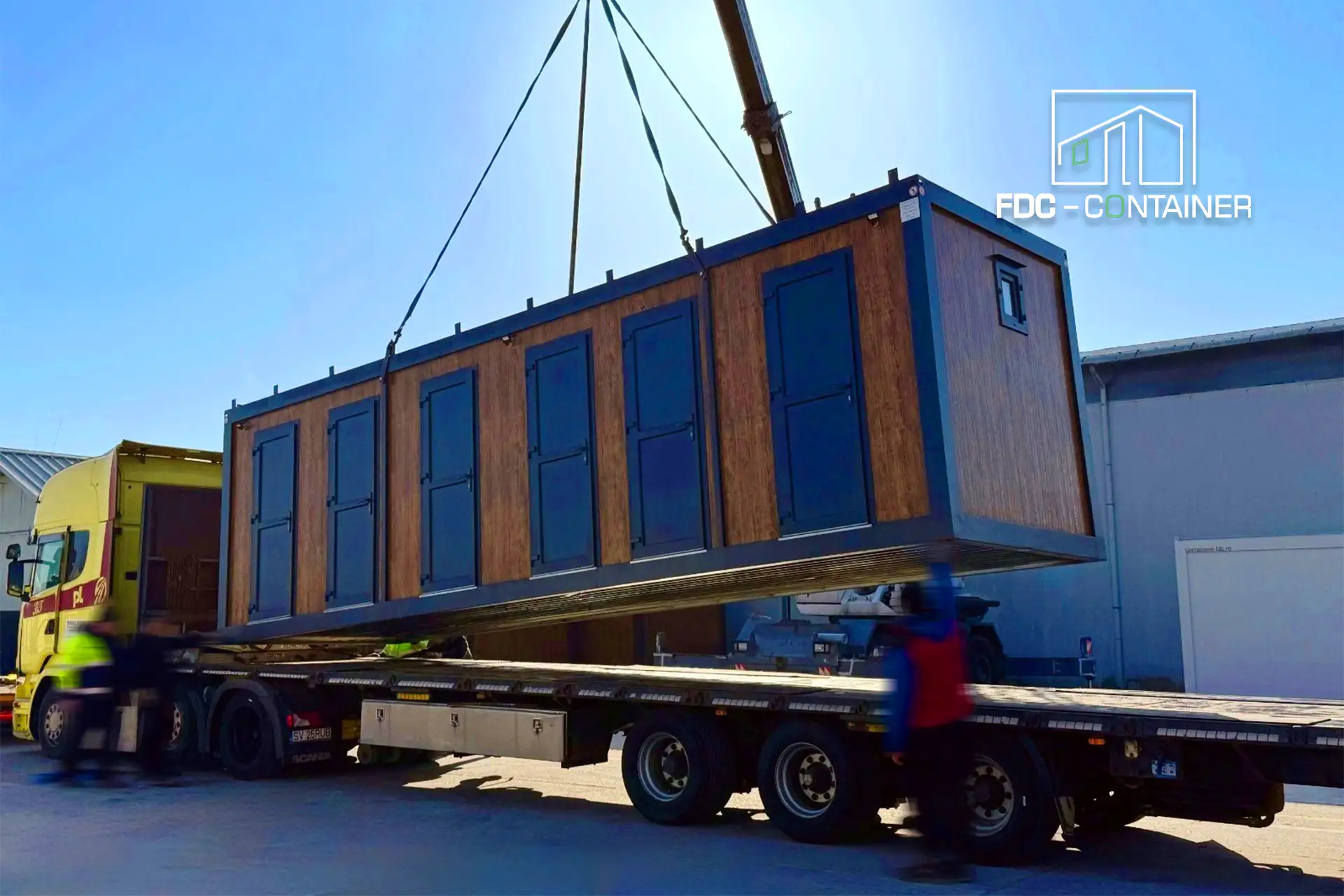 Sanitärcontainer in Holzoptik wird per Kran auf einen Lkw verladen – FDC Container Sanitärcontainer in Holzoptik wird per Kran auf einen Lkw verladen – FDC Container