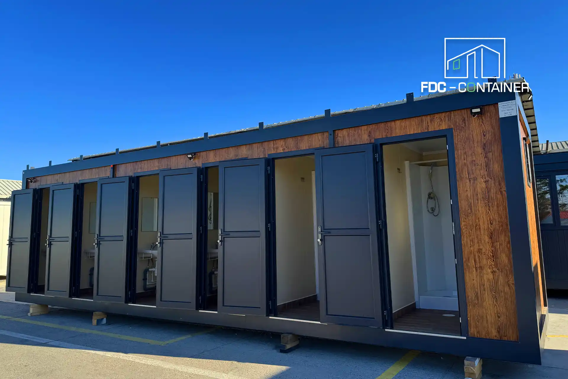 Sanitärcontainer mit Kabinentüren in Anthrazit, eine Tür geöffnet, außen – FDC Container Sanitärcontainer mit Kabinentüren in Anthrazit, eine Tür geöffnet, außen – FDC Container