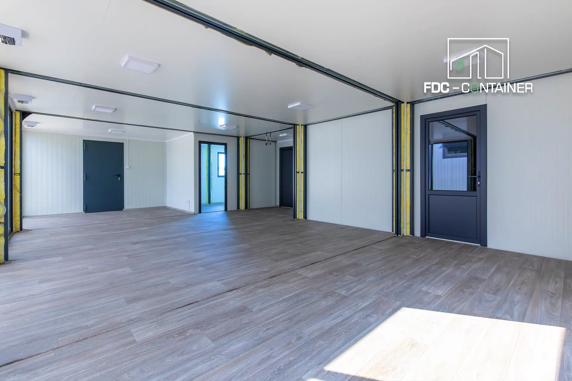 Innenraum einer modularen Büroanlage mit LED-Beleuchtung, getrennten Räumen und großflächigem Bodenbelag - FDC Container