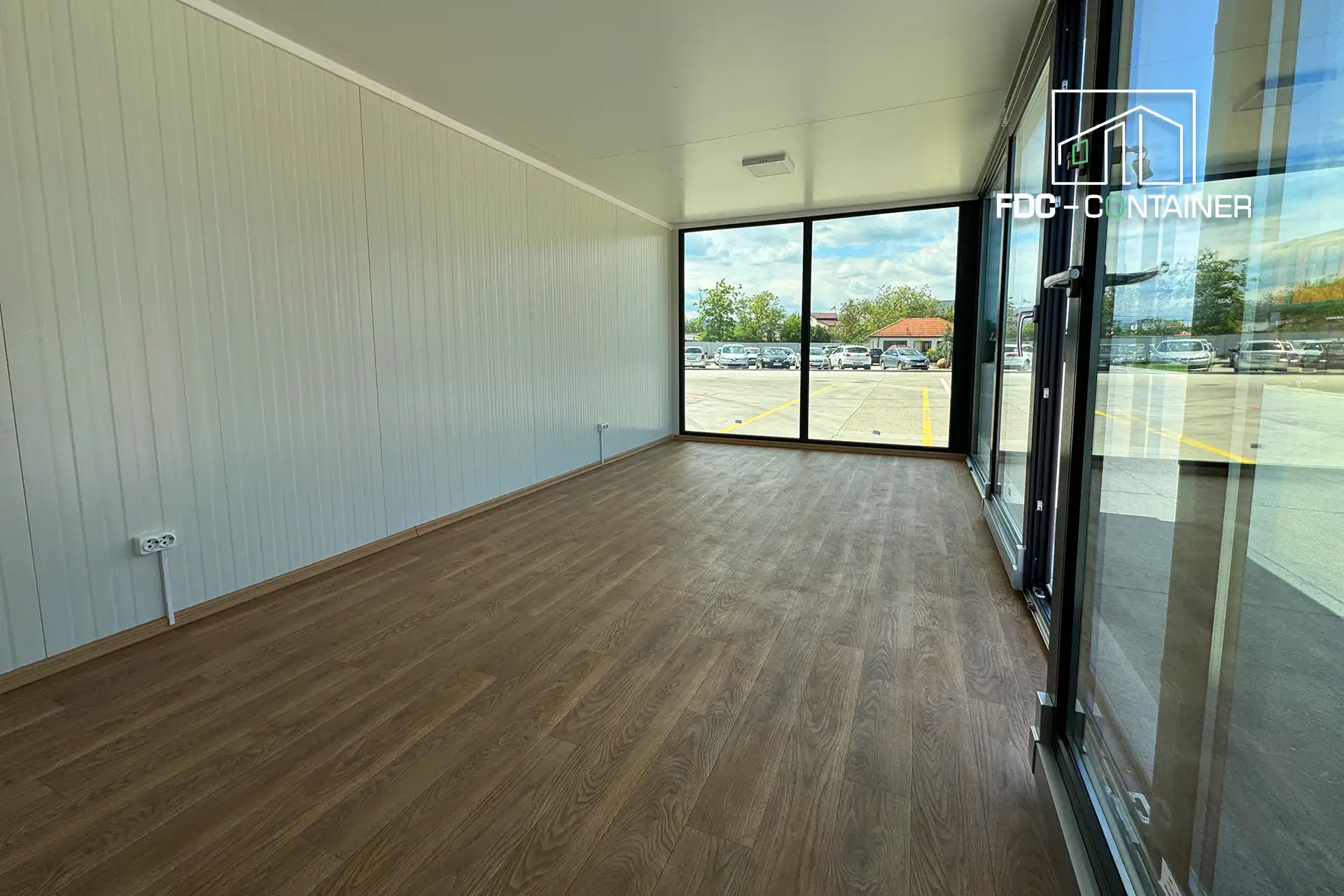 Innenraum eines Bürocontainers mit großen Glasfronten, Holzoptik-Bodenbelag und bereits ab Werk installierter Elektroausstattung - FDC Container