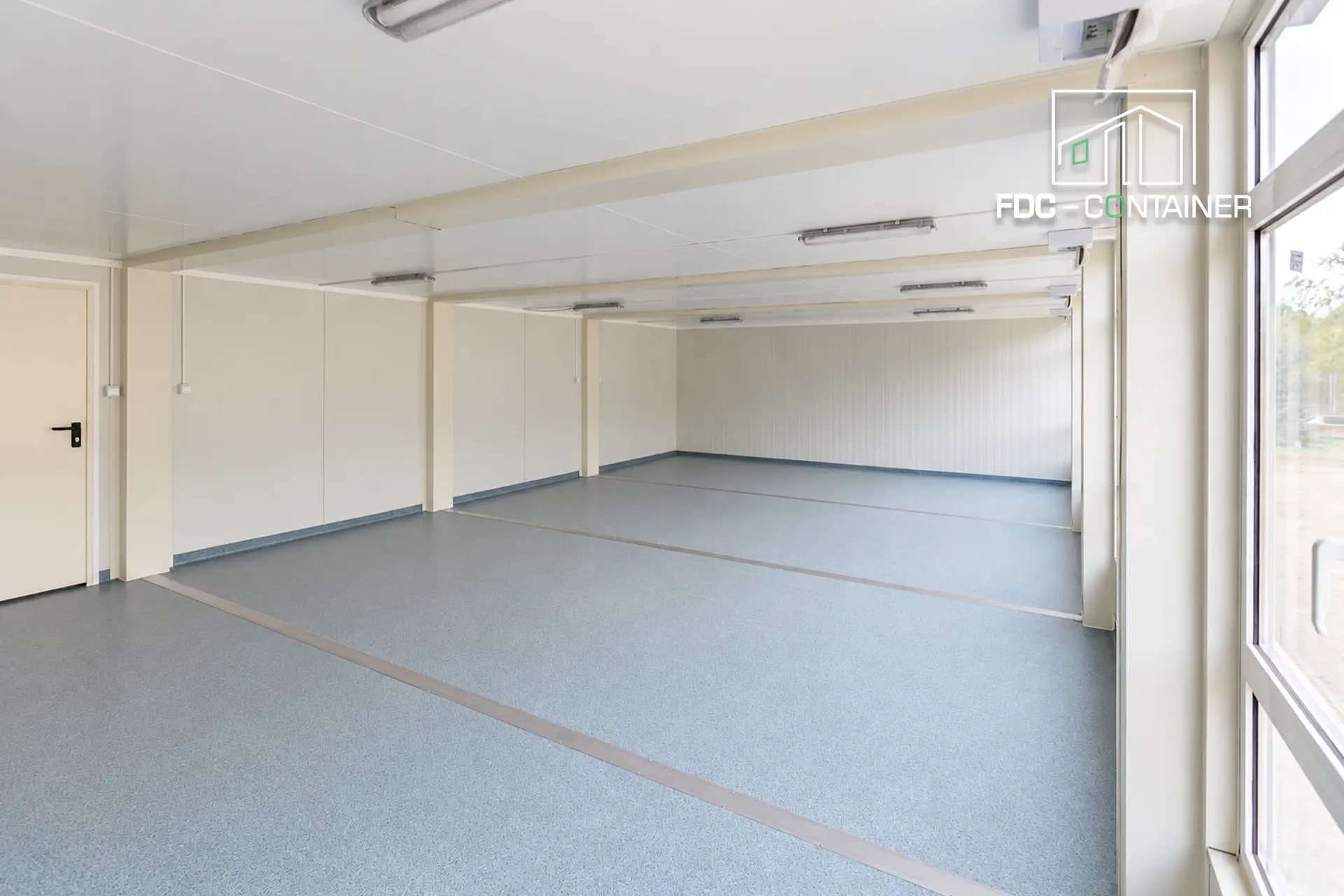Innenraum eines Klassenzimmers aus Containern, ohne Möbel, mit großen Fenstern und grauem Boden - FDC Container